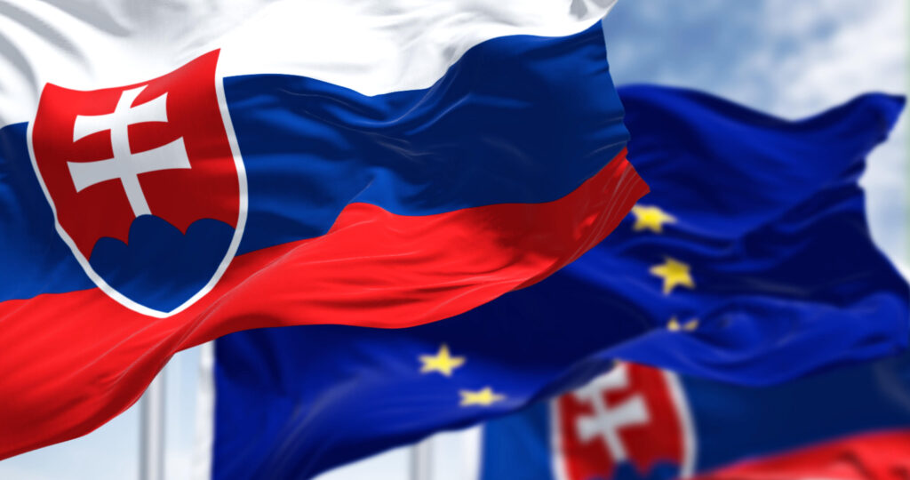 Detail of the national flag of Slovakia waving in the wind with blurred european union flag in the background on a clear day. Democracy and politics. European country.
