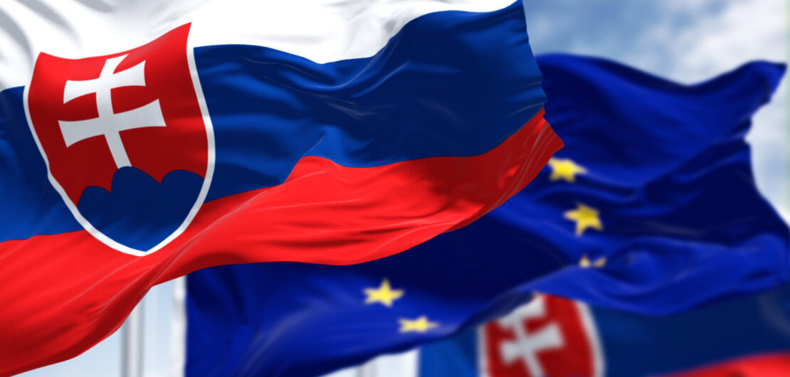 Detail of the national flag of Slovakia waving in the wind with blurred european union flag in the background on a clear day. Democracy and politics. European country.